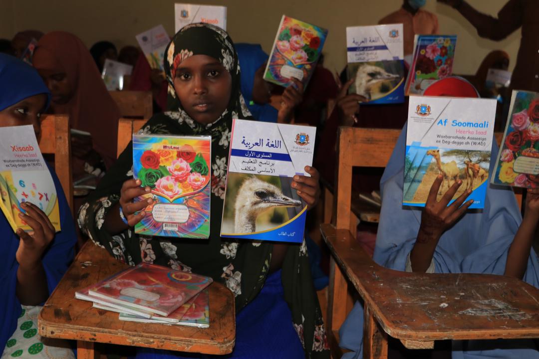 Students in Somalia in a classroom holding up their books.