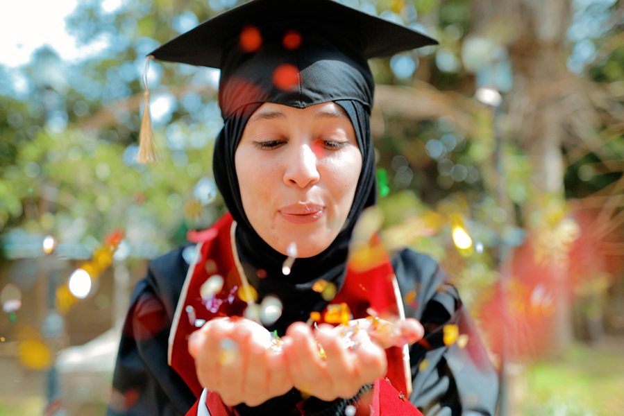 Graduating female student celebrating, blowing glitter at the camera.