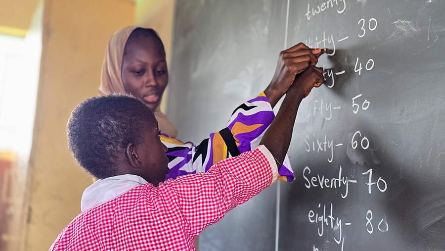 Marie working with her student at the chalkboard in their classroom in Gambia