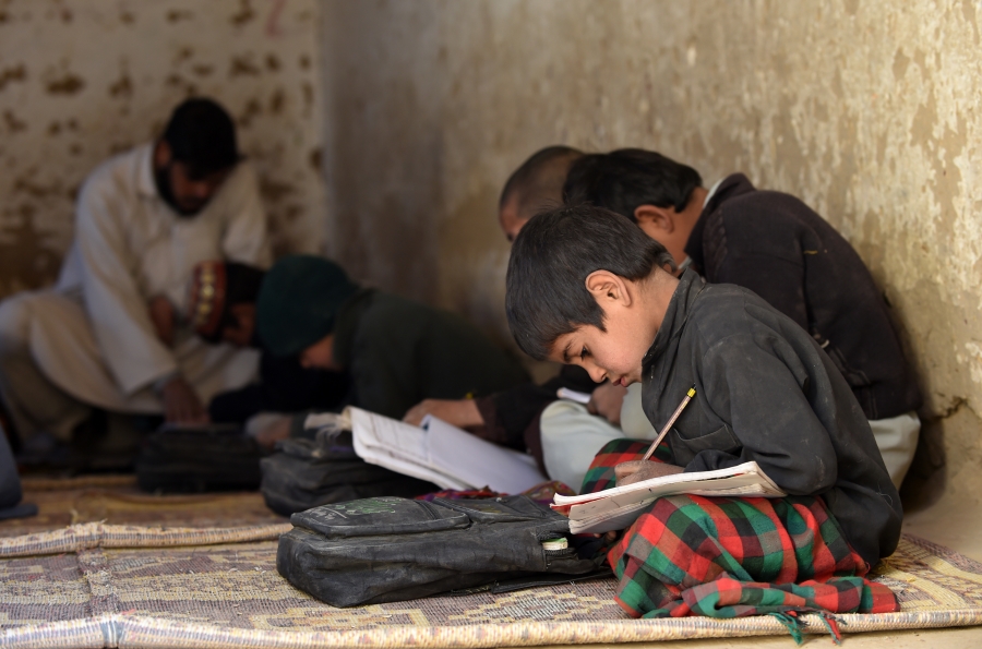 Boys crouched down in the corner of classroom with their workbooks.